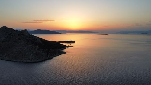 Free A tranquil sunset over a rocky coastline with calm ocean waters. Stock Photo