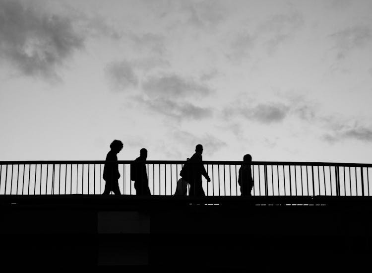 Black And White Photo Of Silhouettes Of People Walking On A Bridge