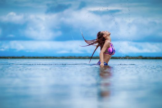 Woman in a colorful bikini splashing water in a serene lake setting, representing carefree summer fun.