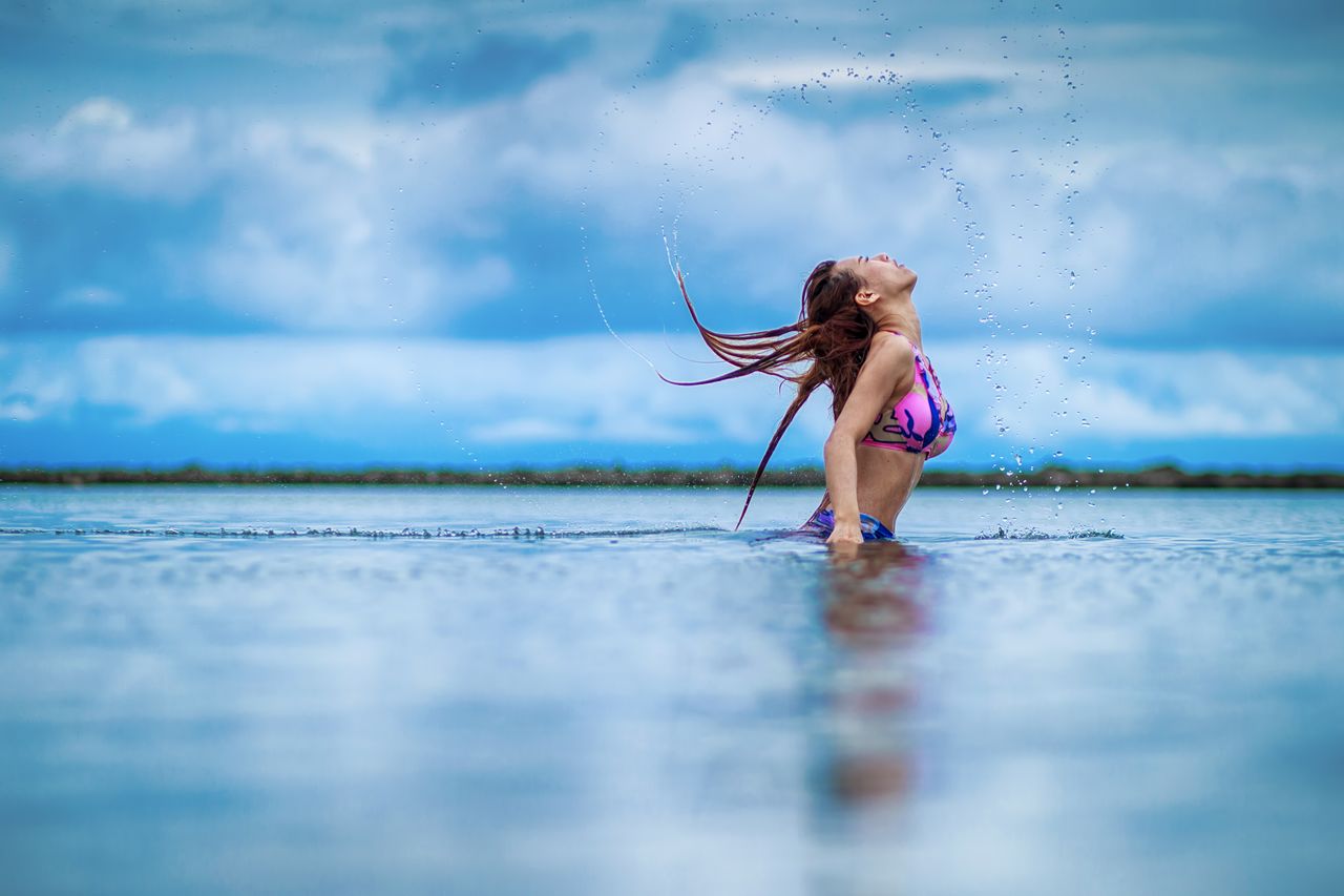 woman in a colorful bikini splashing water in a serene lake setting re