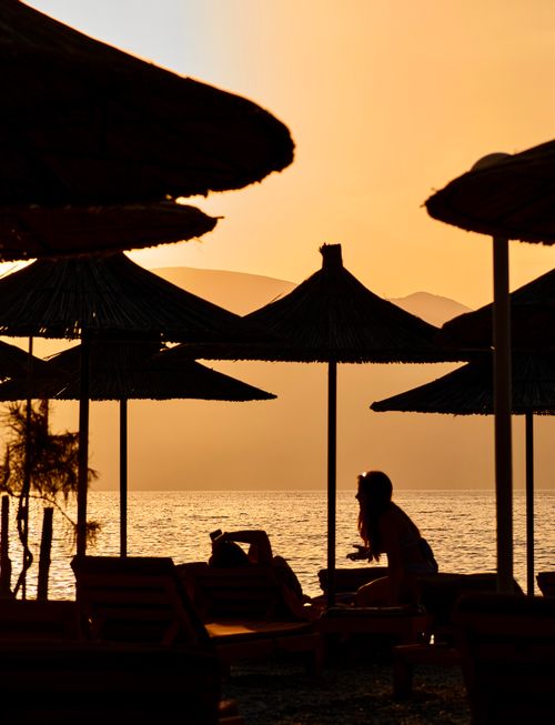 Free Silhouetted figures under umbrellas at sunset in Vlorë, Albania's serene coastline. Stock Photo