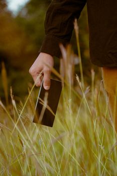 A close-up shot of a person holding a mobile phone in a field of tall grass.