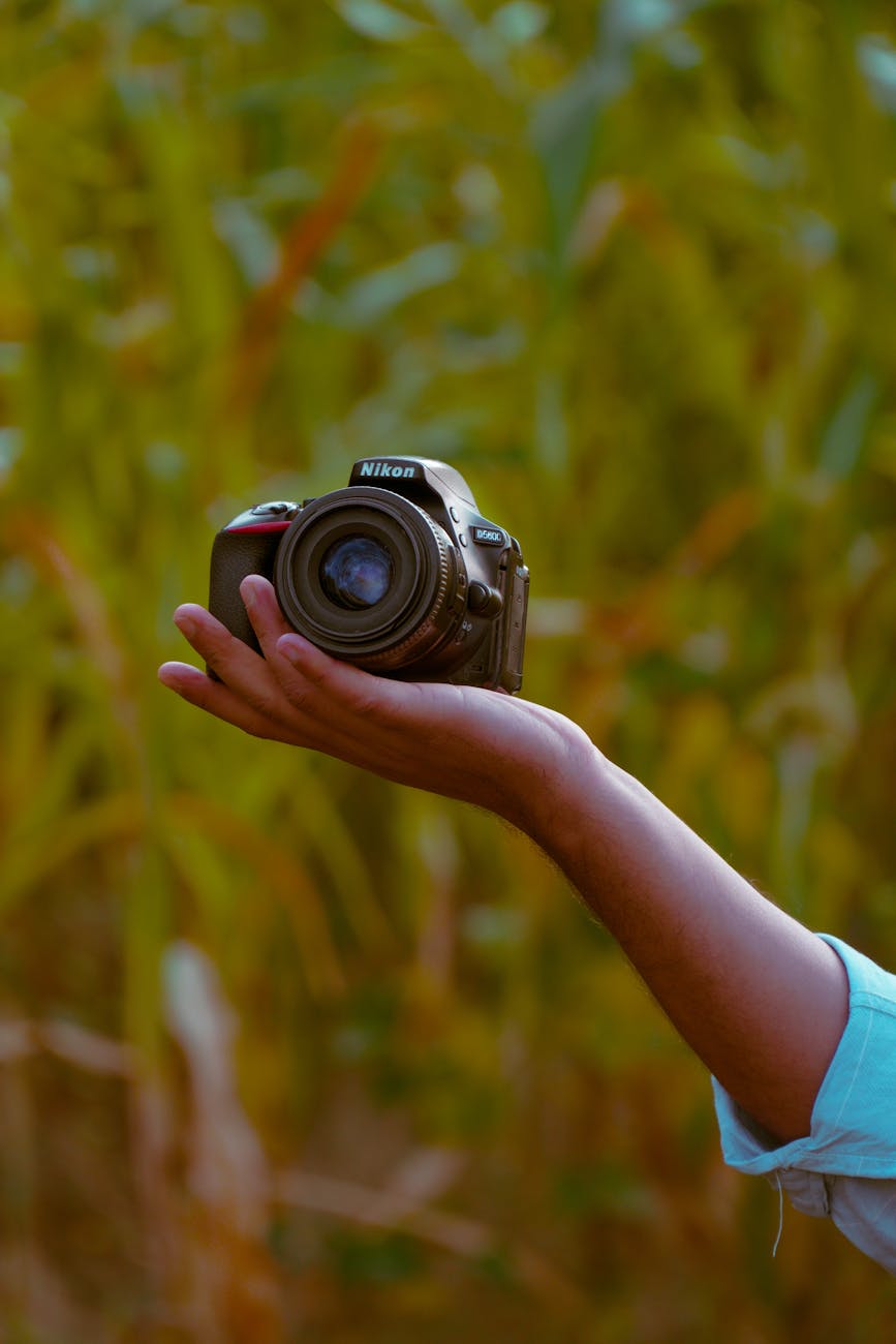 A person holds an SLR camera outdoors, surrounded by greenery. Perfect for nature or photography themes.