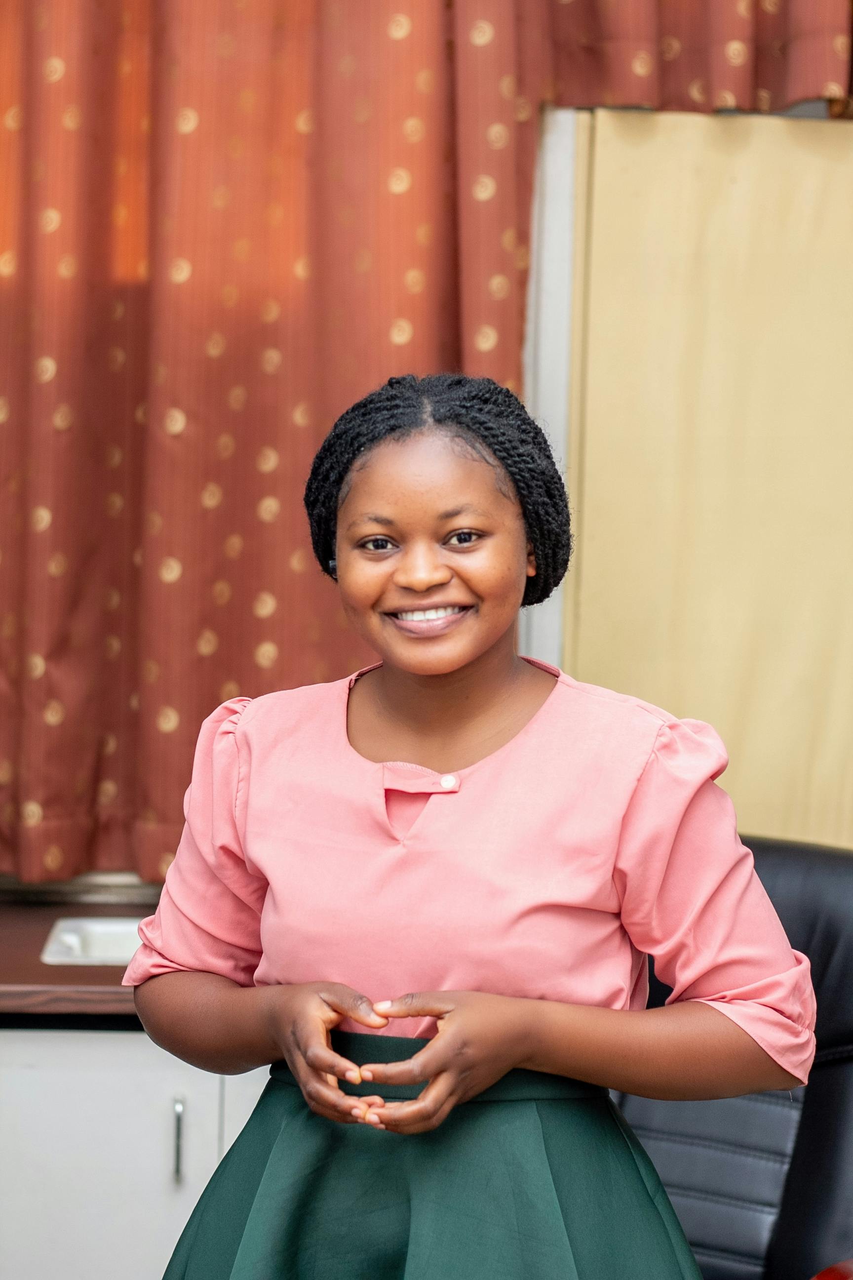 Portrait of a smiling woman in a pink top and green skirt in an indoor setting.