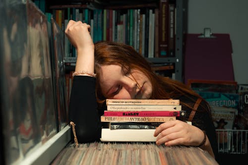 Woman in Black Long Sleeve Shirt Sleeping on Stack of Books