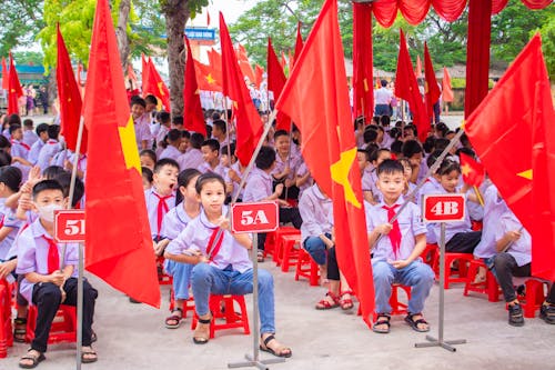 Children Sitting on Red Plastic Chairs