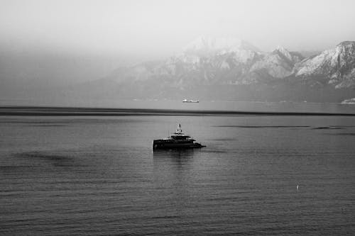 Grayscale Photo of Boat on Sea Near Mountain
