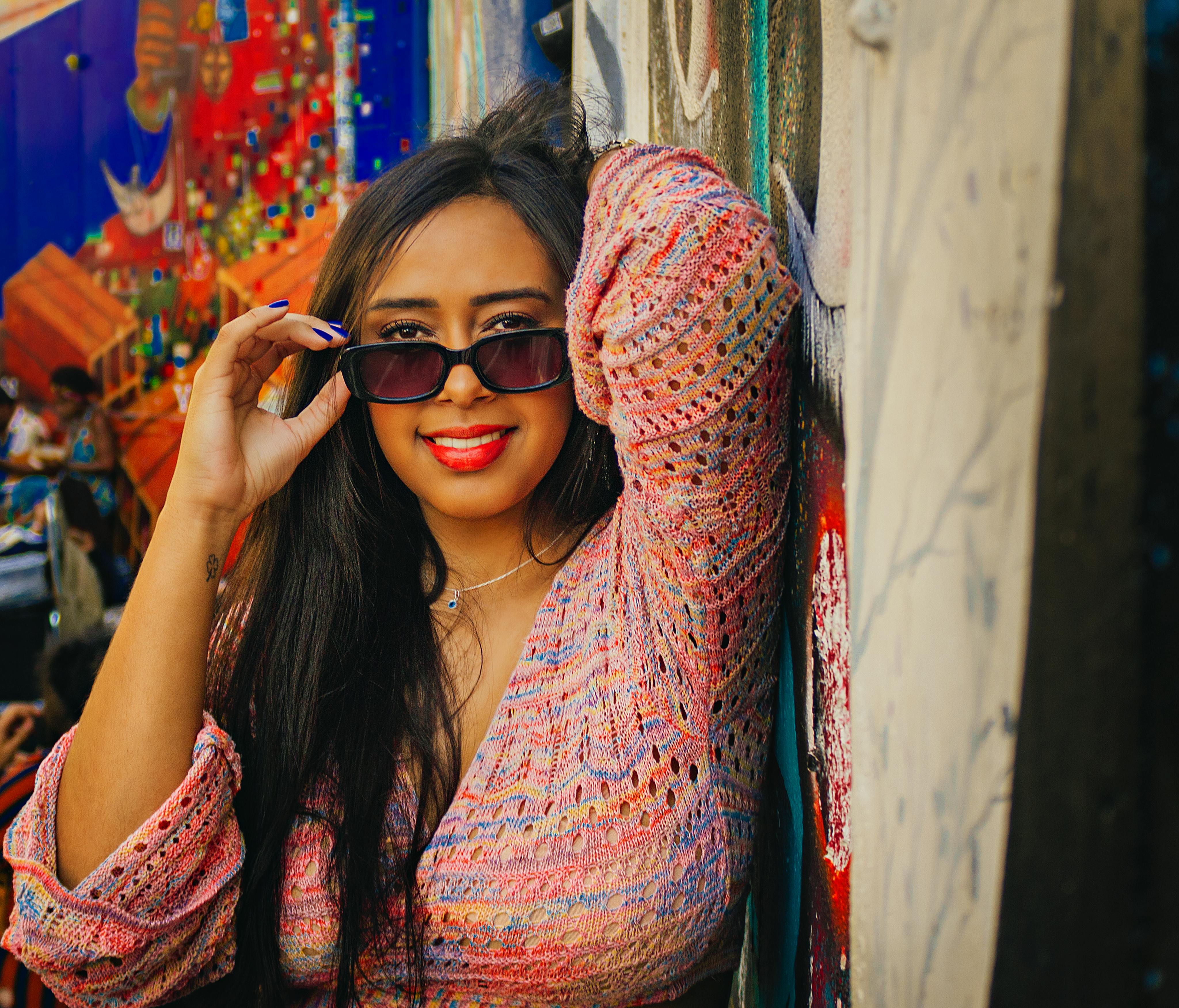 Confident woman in a crochet top posing against a vibrant urban mural, showcasing style and personality.