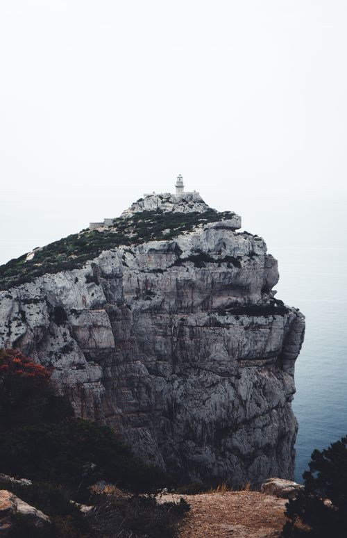 Free Stunning view of a rugged cliff and lighthouse in Alghero, Sardinia, showcasing natural beauty and dramatic landscape. Stock Photo