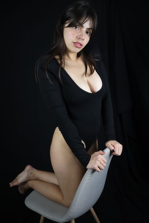 Free A woman in a black outfit posing on a chair in a dark studio setting. Stock Photo