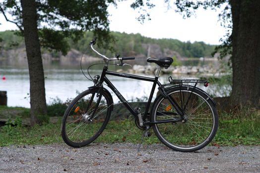 A black bicycle parked on a gravel path by a tranquil lakeside in Stockholm, Sweden.