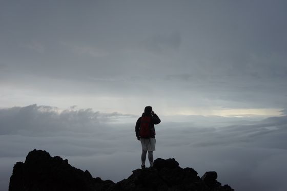 Lone climber standing on a mountain peak above the clouds — photo by The Duluwa on Pexels
