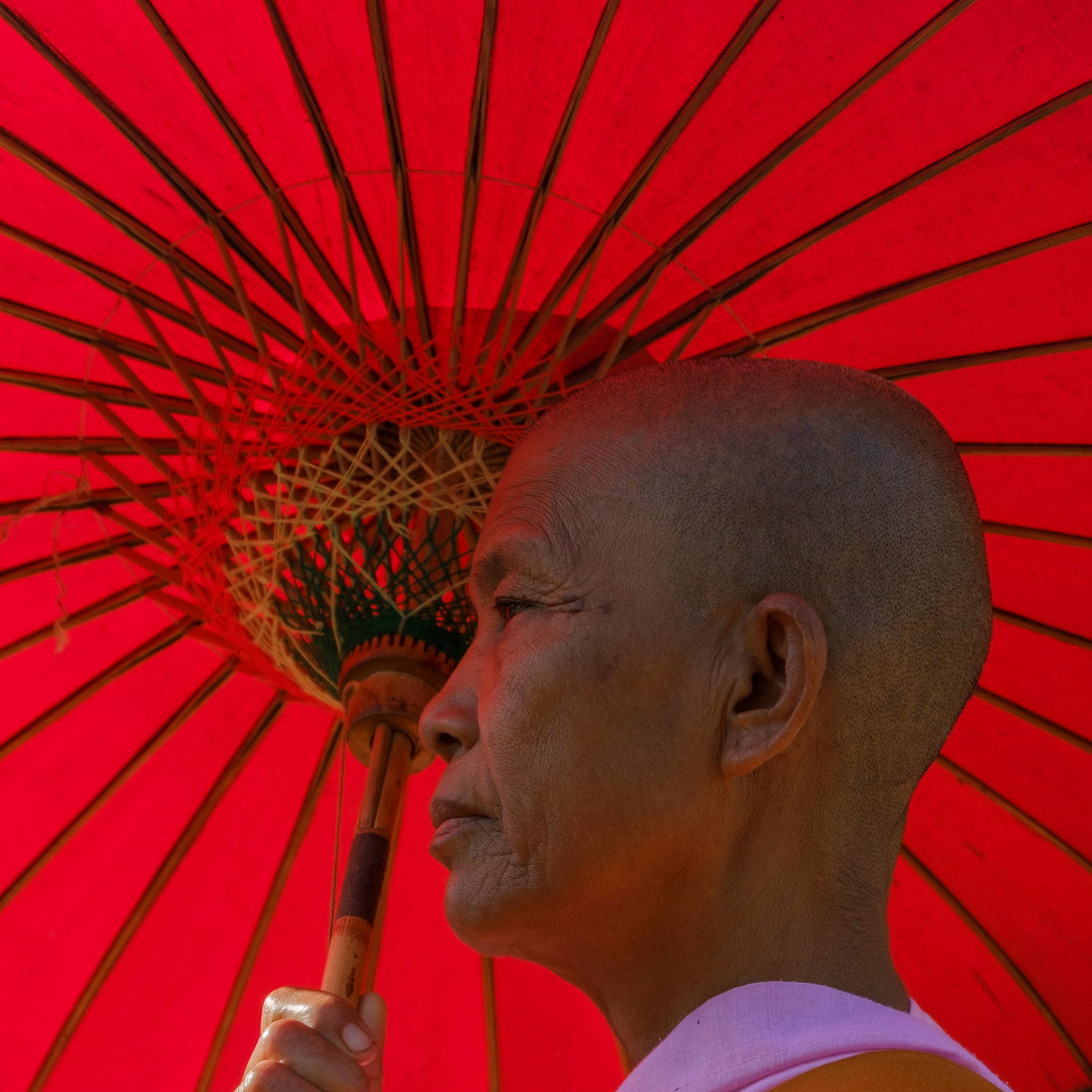 Close-up portrait of an elderly man holding a vibrant red umbrella.