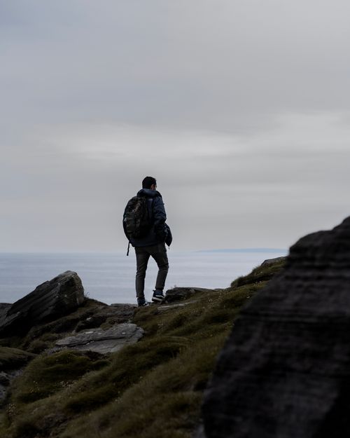 Free A lone hiker with a backpack enjoys the scenic ocean view from a rocky cliff. Stock Photo