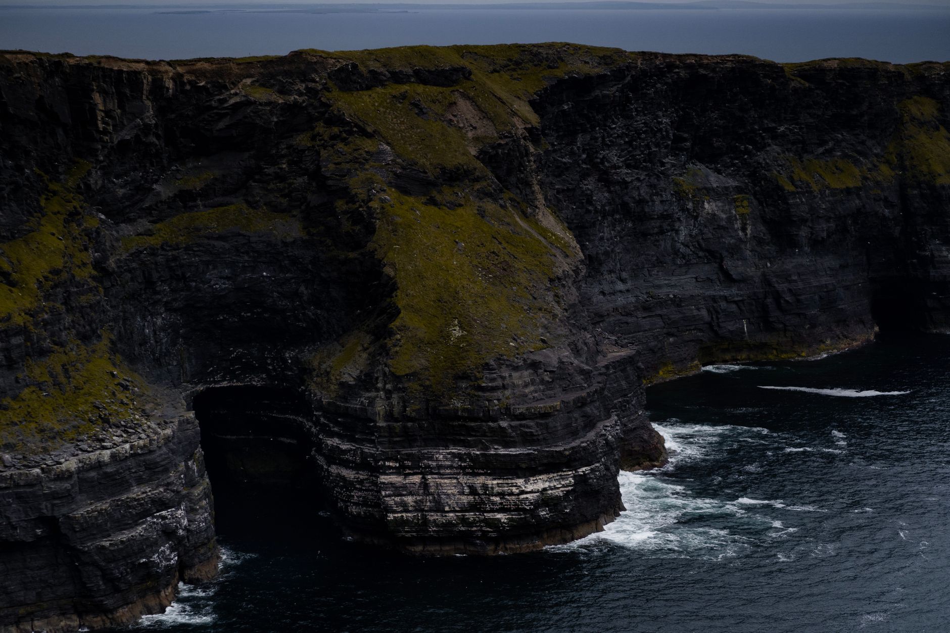 Stunning view of rugged cliffs with ocean waves crashing below on a gloomy day.