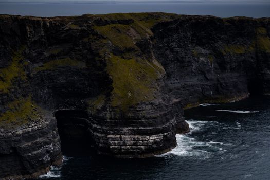 Stunning view of rugged cliffs with ocean waves crashing below on a gloomy day.