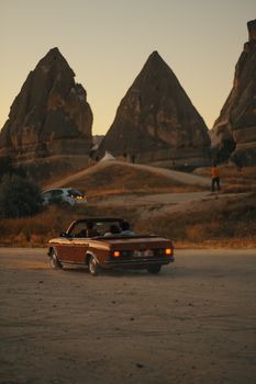 Capture of a vintage convertible driving through Cappadocia with sunset-lit rock formations.