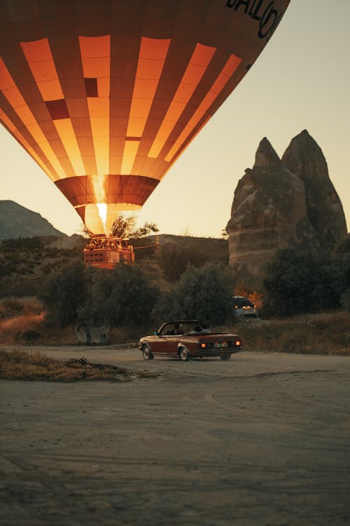 A Hot Air Balloon Flying near a Red Convertible Car