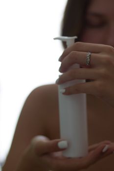 Woman with a ring dispensing cosmetic product from a bottle with a pump.
