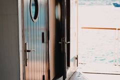 Interior view of a ship showing wooden doors with portholes and a sea view through open doors.