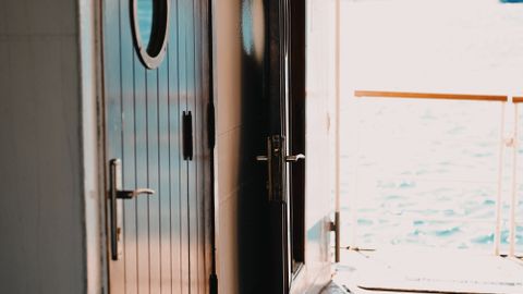 Interior view of a ship showing wooden doors with portholes and a sea view through open doors.