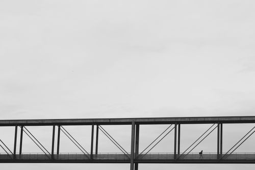 Free Black and white photo of a lone person crossing a minimalist bridge. Stock Photo