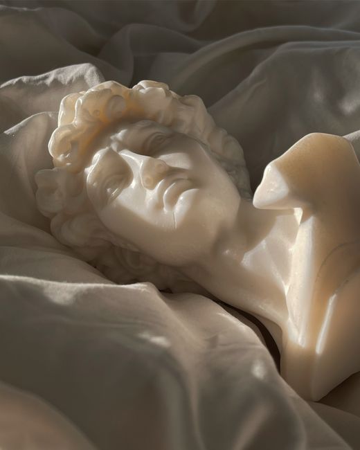 Elegant marble bust laying on satin fabric, showcasing artistic craftsmanship under soft lighting.