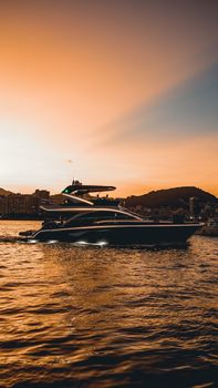 A luxury yacht cruising in a scenic harbor at sunset with a vibrant sky and calm waters.