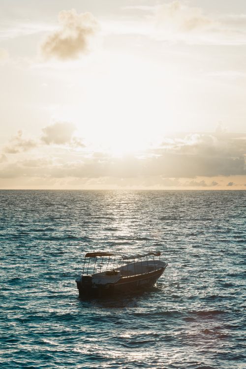 Free A solitary boat floats on a shimmering sea under a serene sunset, creating a tranquil scene. Stock Photo