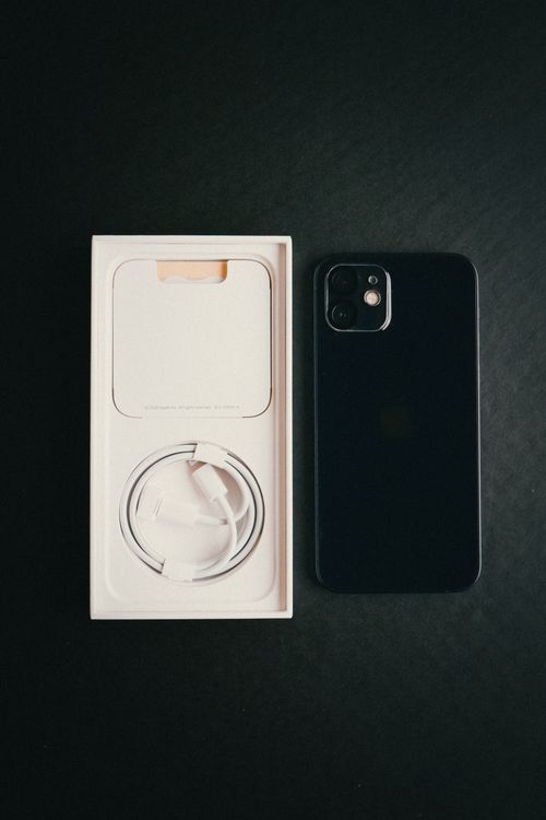 Free High-angle shot of a smartphone, charger cable, and box on a dark surface. Stock Photo