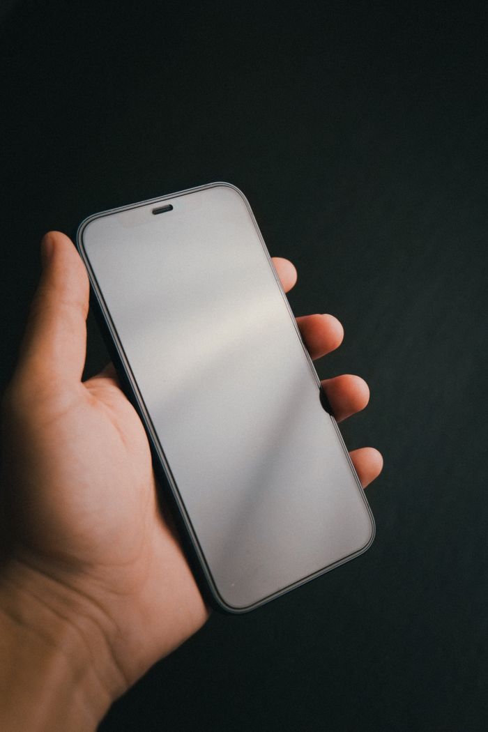 A hand holding a phone against a dark background — Luis Quintero on Pexels