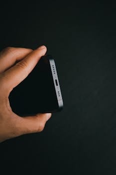 A detailed view of a smartphone being held against a dark background, showcasing its sleek design.