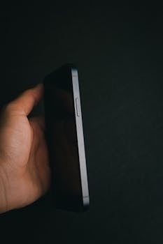 A close-up of a hand holding a smartphone with a dark background, emphasizing modern technology.