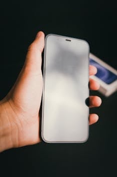 A person holding a smartphone with a reflection on the screen against a black background.