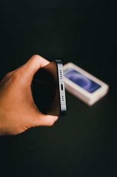Detailed view of a smartphone held in hand, focusing on the lightning port, with packaging blurred in the background.