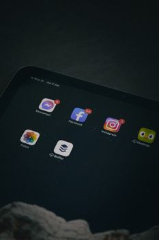 Close-up of a tablet screen displaying social media apps in a dim setting.