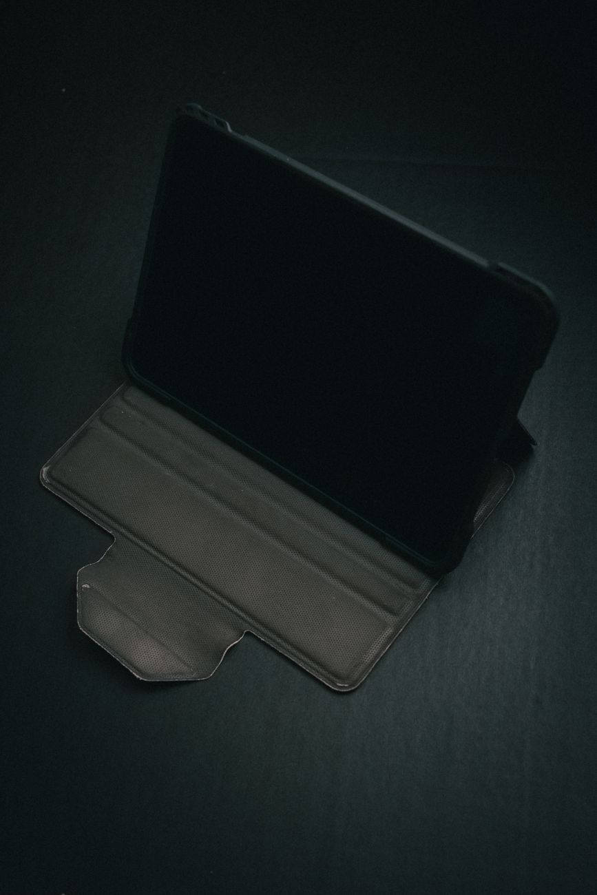 A black tablet in an open protective case, viewed from above on a dark background.