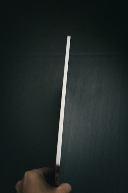 A tight focus on a person holding a tablet showing its thin side profile against a dark background.