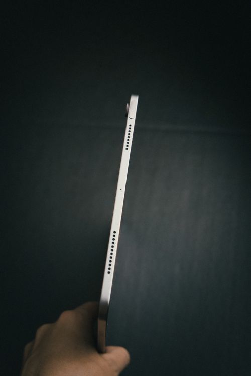 Free Side view of a person holding a tablet, focused on the slim profile against a dim background. Stock Photo