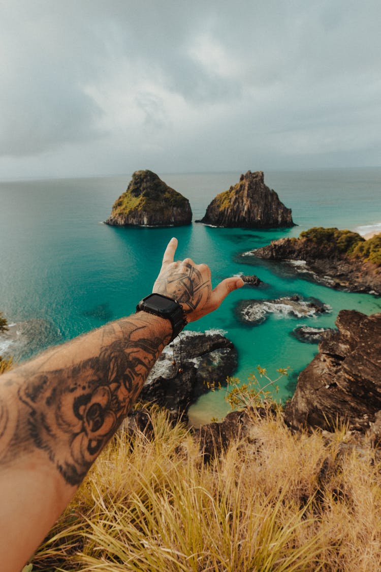 Mans Tattooed Arm Against The Islands Of Baia Dos Porcos, Brazil