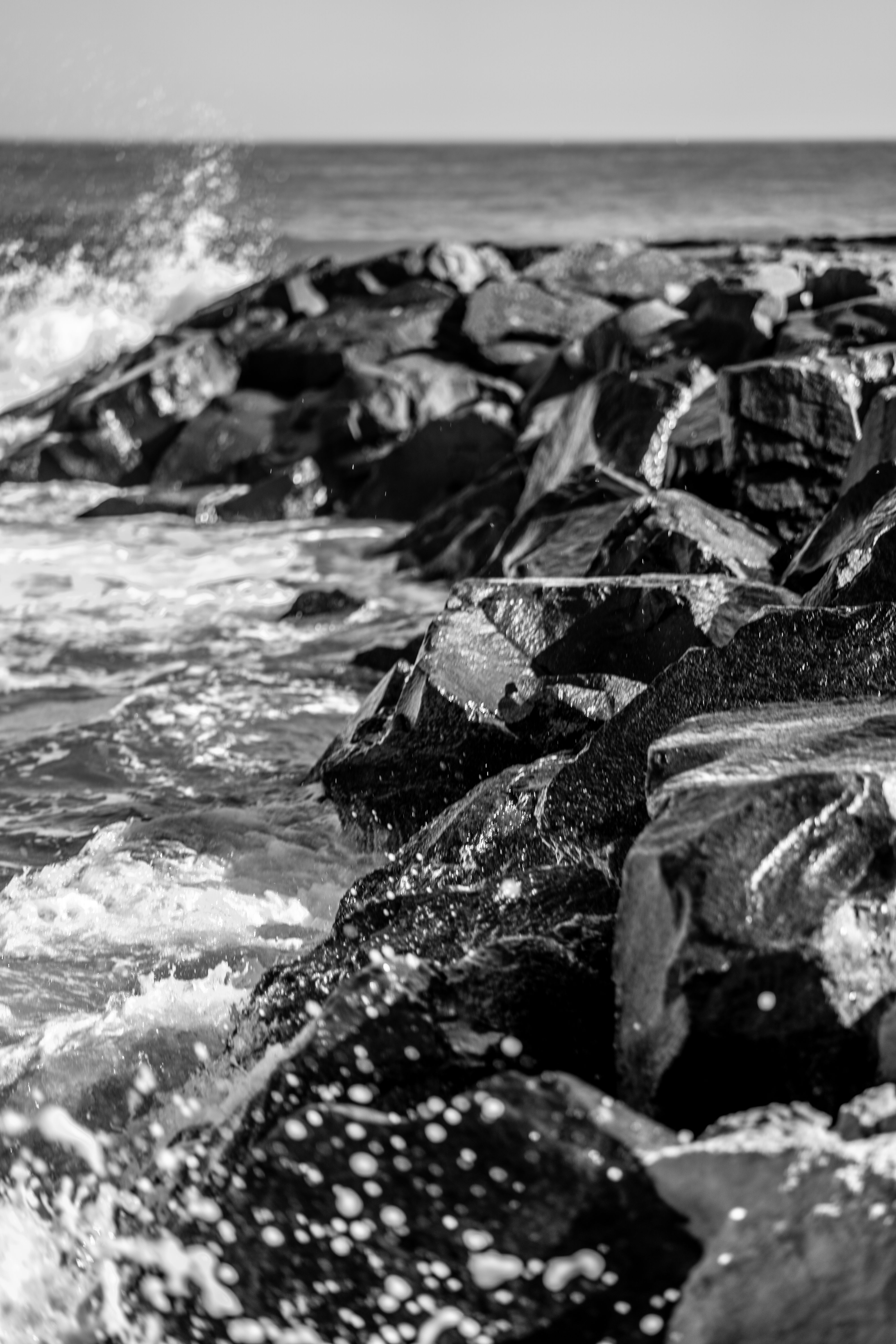 Dynamic black and white image of ocean waves crashing on rugged rocks.