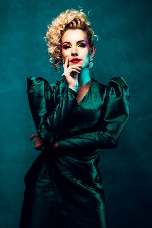 Free Striking fashion portrait of a woman in a green dress with bold makeup and curly blonde hair. Stock Photo