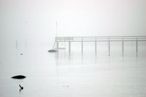 Free A serene image of a wooden pier extending into foggy, still waters. Stock Photo
