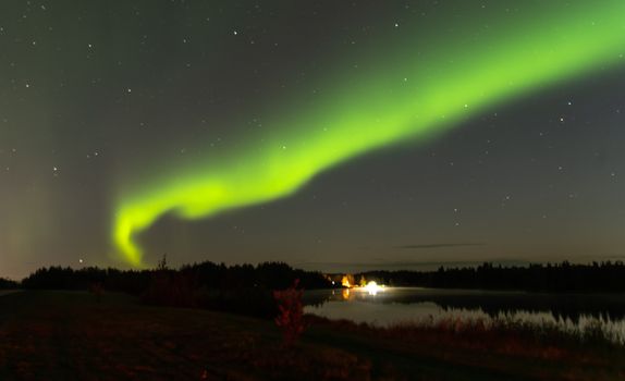 Vibrant Northern Lights illuminating a serene Alaskan night sky over a tranquil lake.