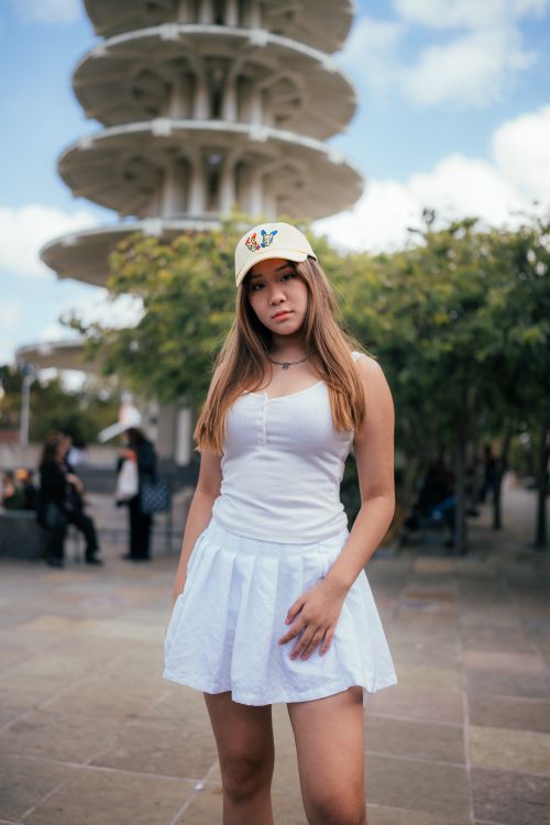 Free Asian woman posing near a pagoda in casual sportswear, white skirt, and cap. Stock Photo