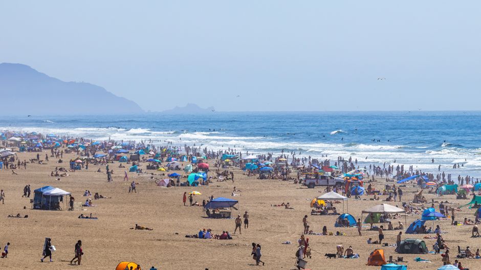 Crowded beach scene with people relaxing and swimming on a sunny summer day.