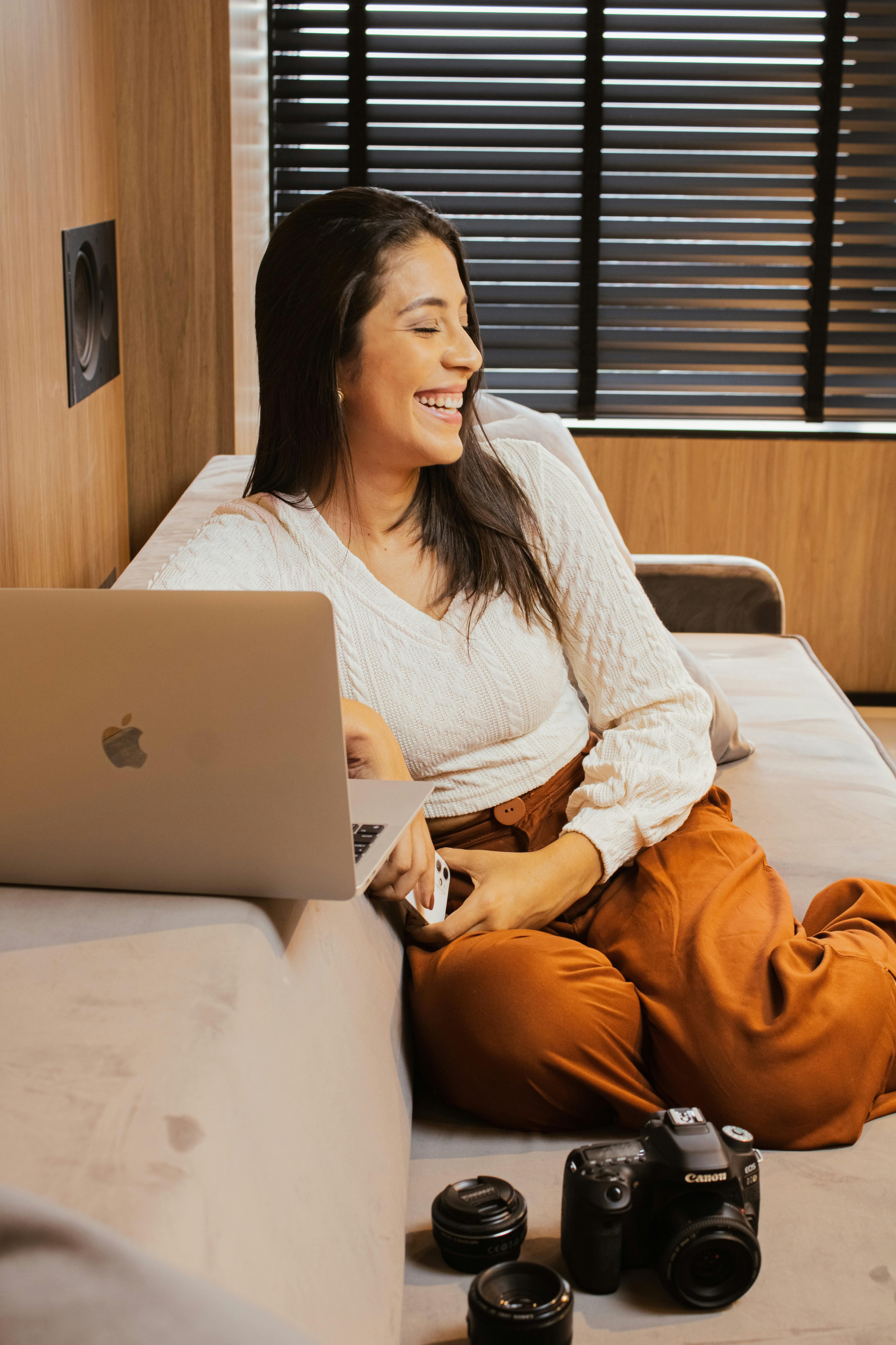 Free Woman in White Sweater and Orange Pants Sitting on Bed Using Macbook Stock Photo