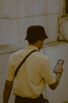 A man wearing a bucket hat uses his smartphone while walking outside in Istanbul, Turkey.