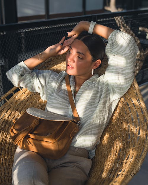 Woman in White and Gray Stripe Long Sleeve Shirt Sitting on Brown Wooden Chair