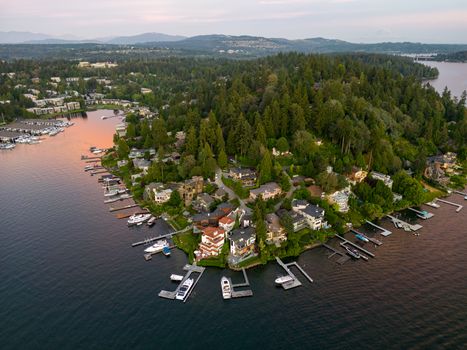 Scenic aerial view of waterfront homes, marina, lush greenery, and distant mountains during sunset.